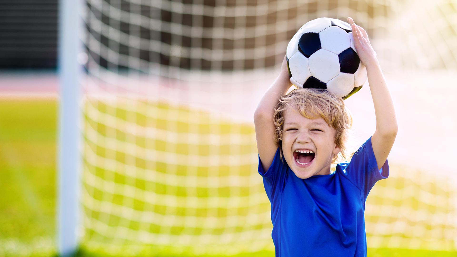 Kids play football on outdoor stadium field. Children score a goal during soccer game. Little boy kicking ball. School sports club. Training for young player.